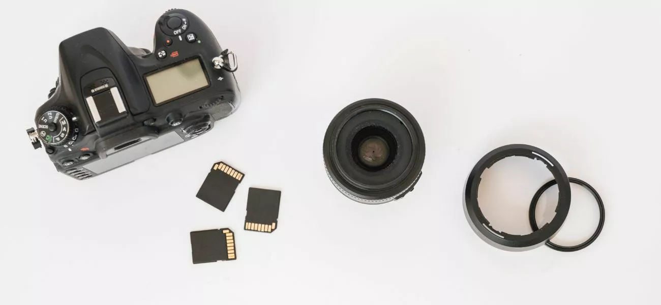Foto de uma máquina fotográfica vista de cima com sua lente e cartões de memória ao redor